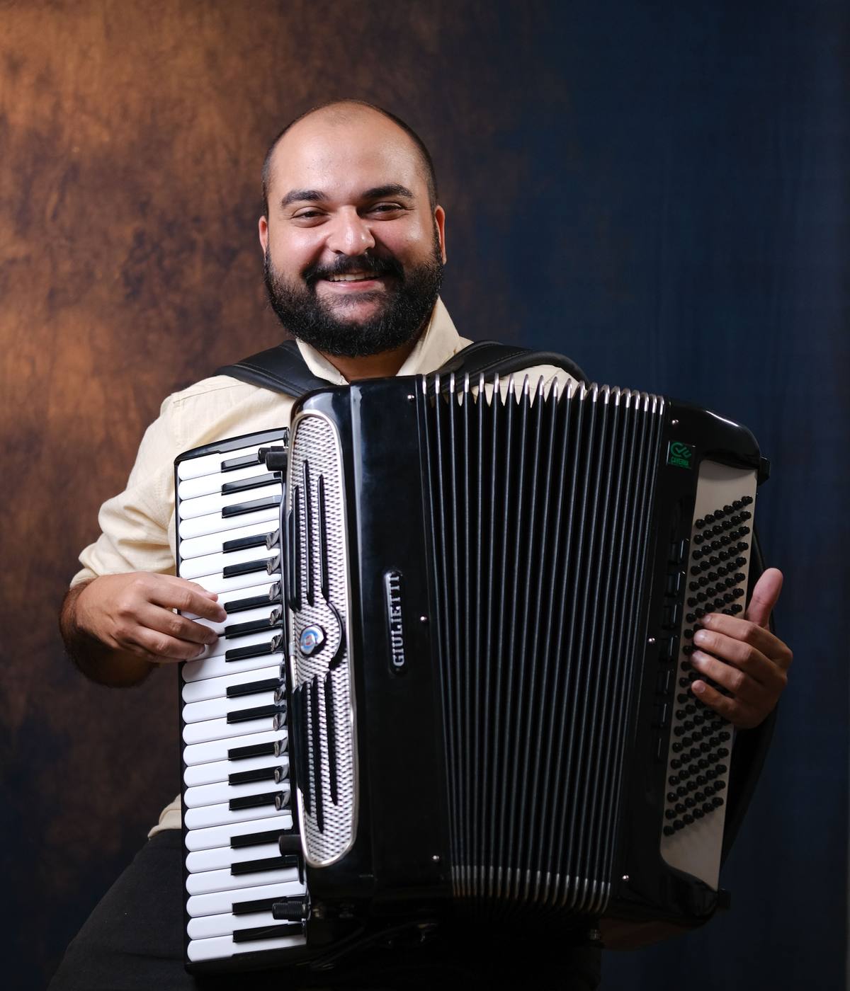 Ranier Oliveira sorrindo, em busto, com sua sanfona Giulietti, emergindo da escuridão de palco