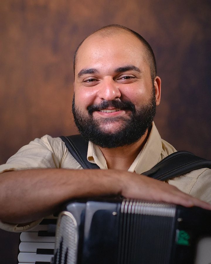 Retrato de Ranier Oliveira sorrindo, apoiado sobre a sanfona